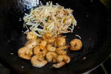 Sauteeing shrimp with shallots in a wok