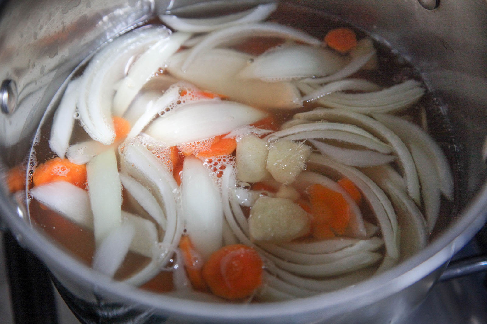 Carrots, onions, ginger added to broth for Easy Nutritious Chicken Vegetable Soup with Noodles in Bone Broth. Have it to treat covid-19 at home.