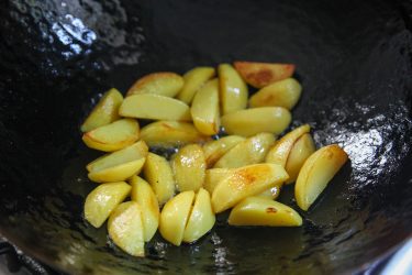 sautéing potatoes in a wok, before green garlic is added
