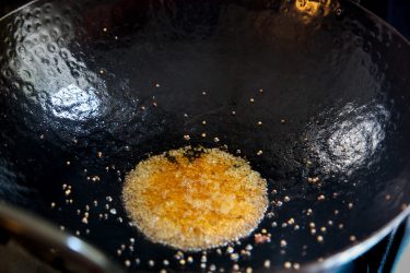 yellow mustard seeds popping in hot oil in a wok, before green garlic is added