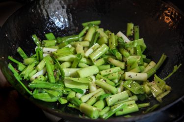 sliced green garlic added to wok with mustard seeds
