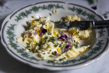 adding flowers and herbs to butter in a shallow bowl