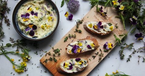 Herb butter with edible flowers in a bowl and slices of baguette spread with butter, ready to eat