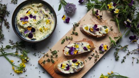 Herb butter with edible flowers in a bowl and slices of baguette spread with butter, ready to eat