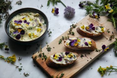 Herb butter with edible flowers in a bowl and slices of baguette spread with butter, ready to eat