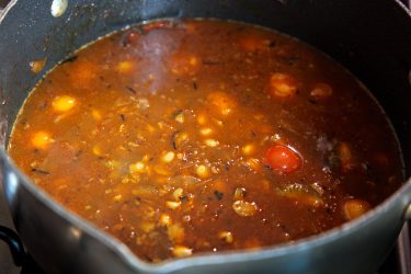 Cherry tomatoes and water added to pot with ingredients
