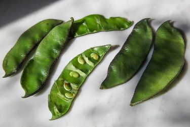 Fresh Sheem or Hyacinth Bean pods, with one cut open to show the seeds or bichi inside