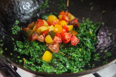 Cherry tomatoes added to stir-fried kale in a wok