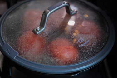 Tomatoes cooking in a little oil in a pan, covered with lid