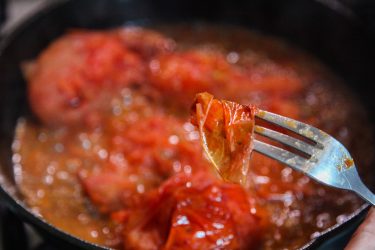 Removing peel with a fork from disintegrated tomatoes in pan