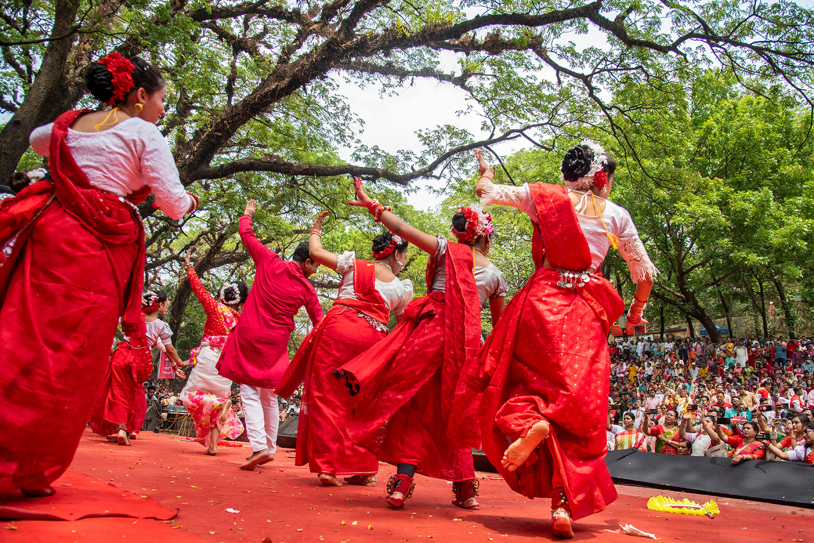 Women in red saris dancing on stage in front of audience at at large outdoor festival in Bangladesh for Pohela Boishakh